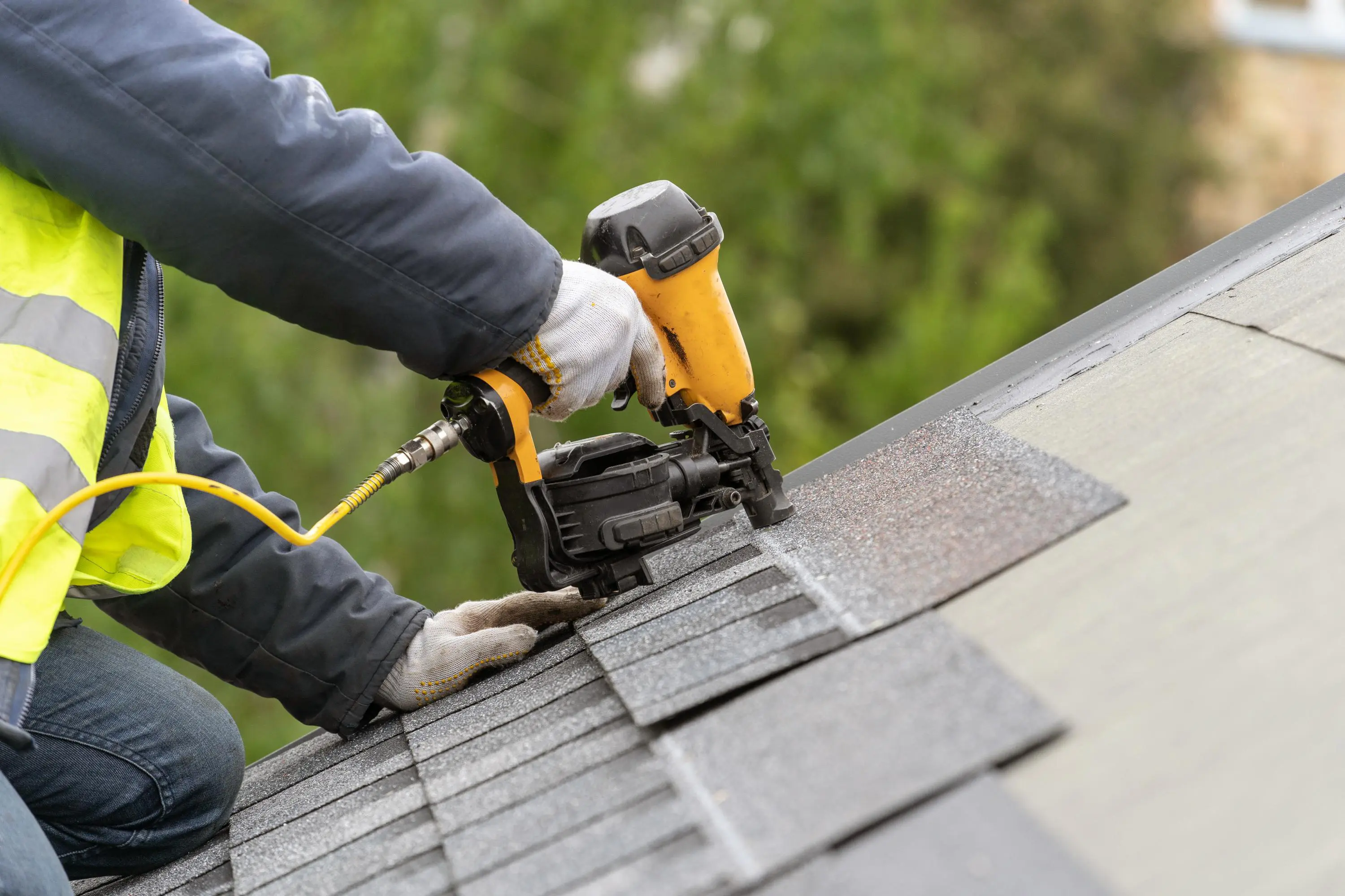 Worker using nail gun on roof shingles.