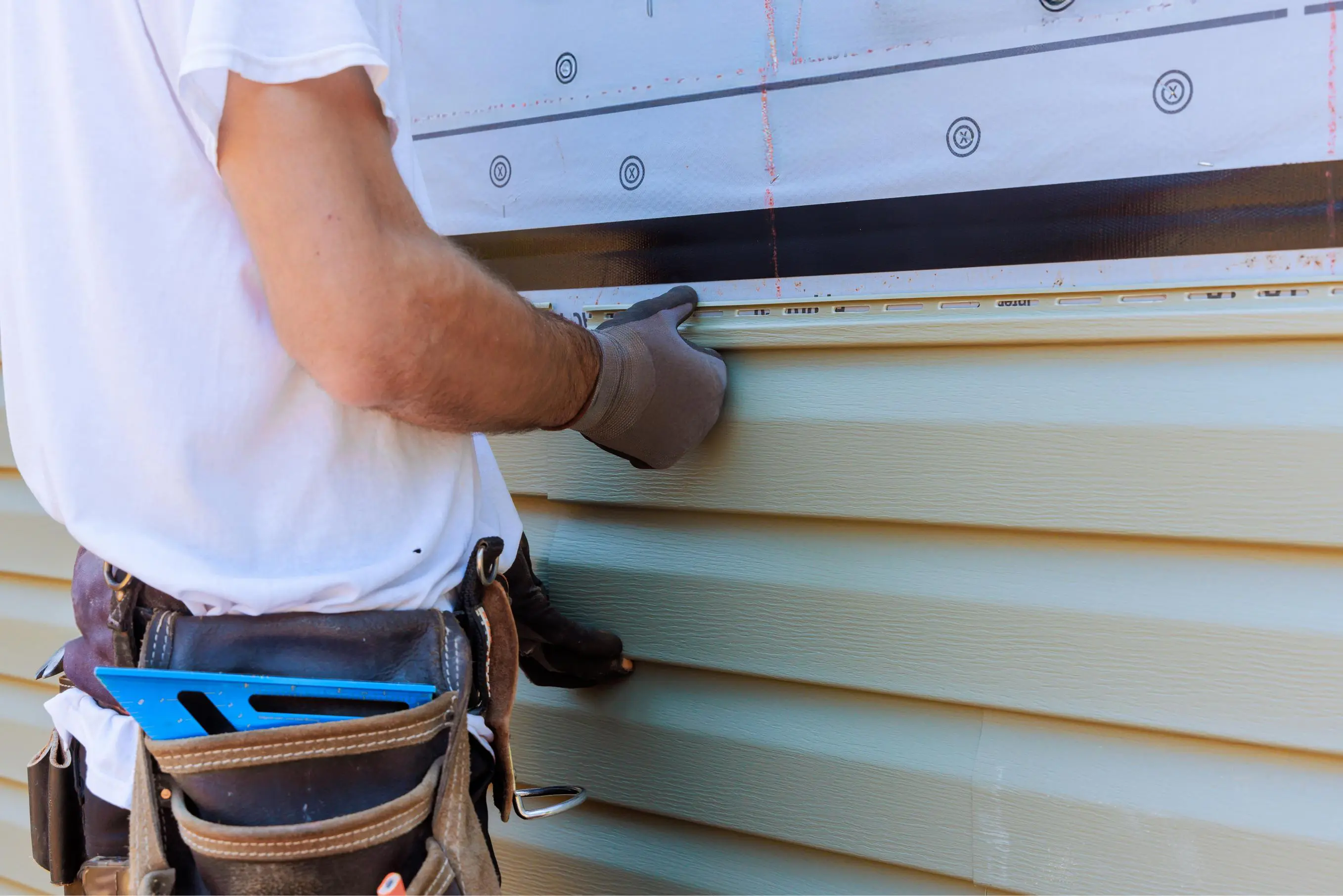 Worker installing vinyl siding on house.