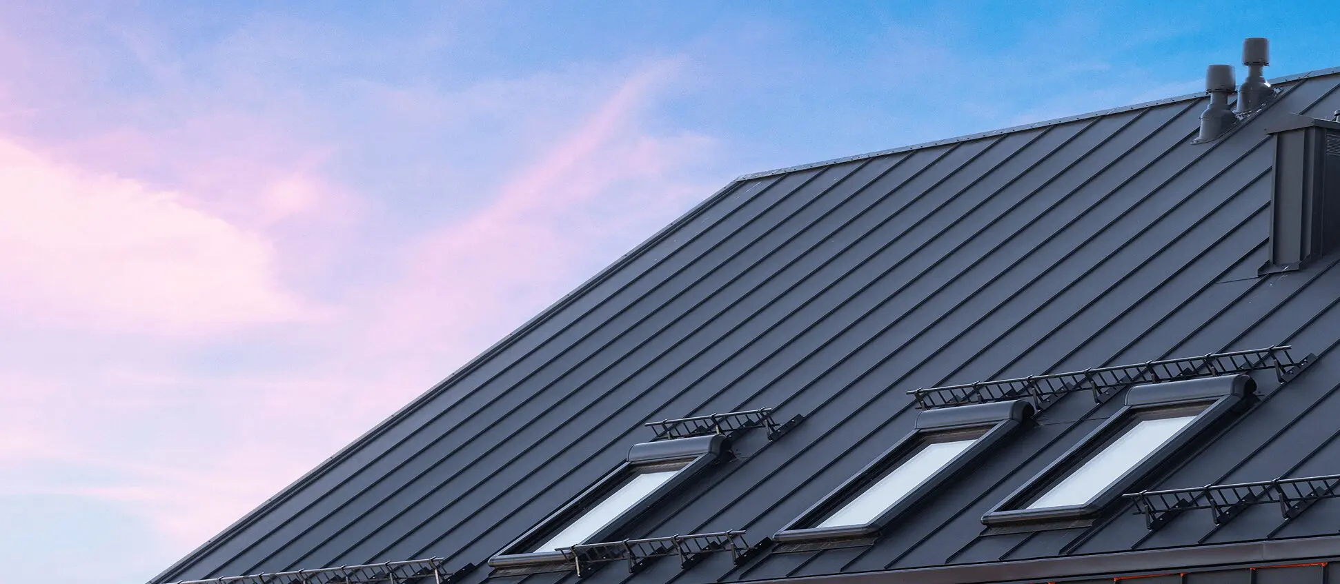Modern metal roof with skylights at sunset.