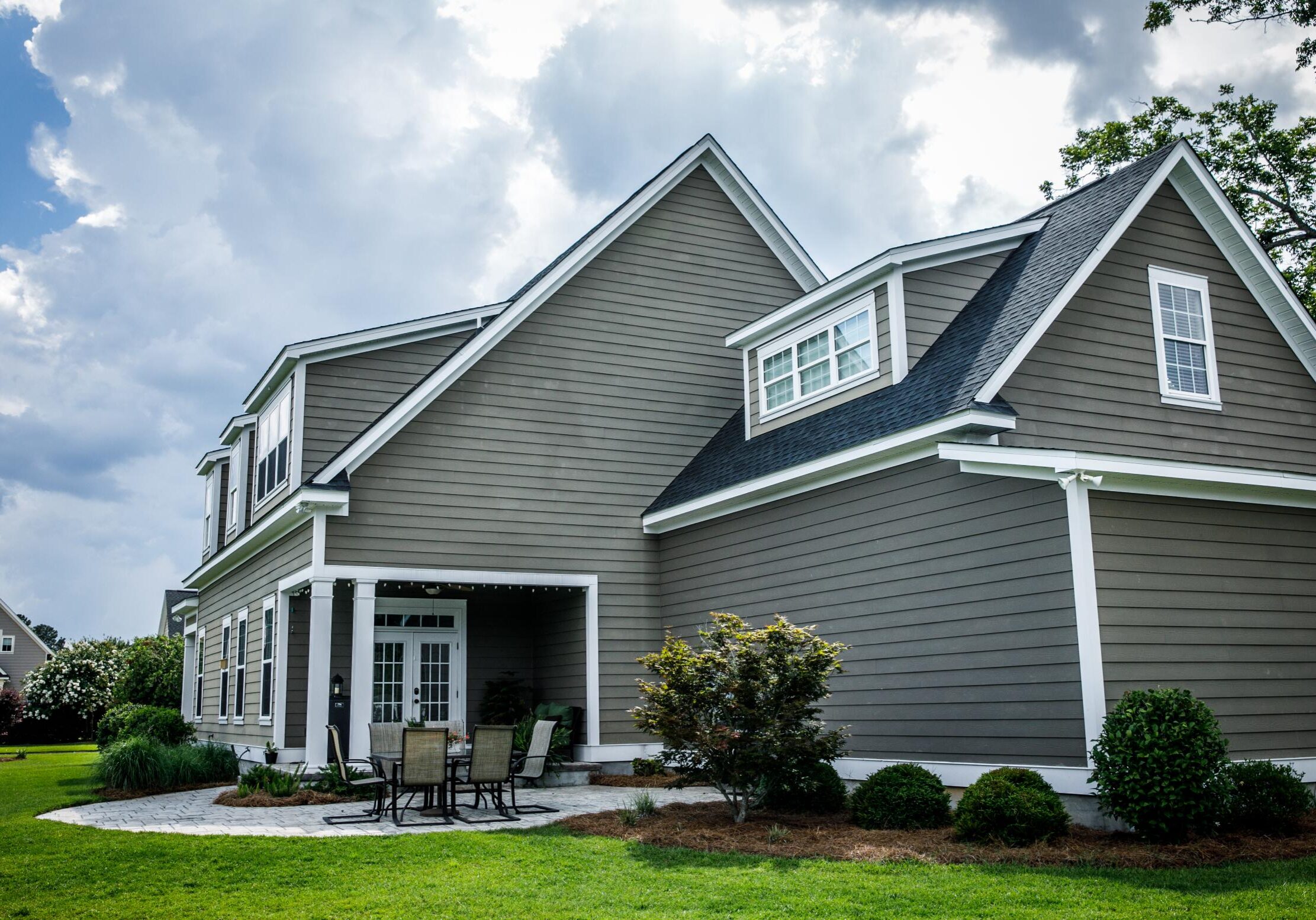 Gray house with patio and cloudy sky.