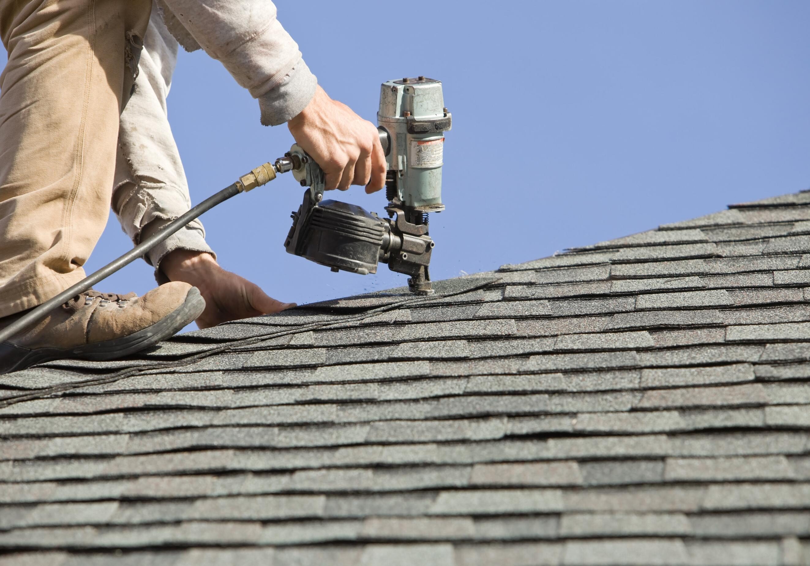 Worker using nail gun on roof shingles.