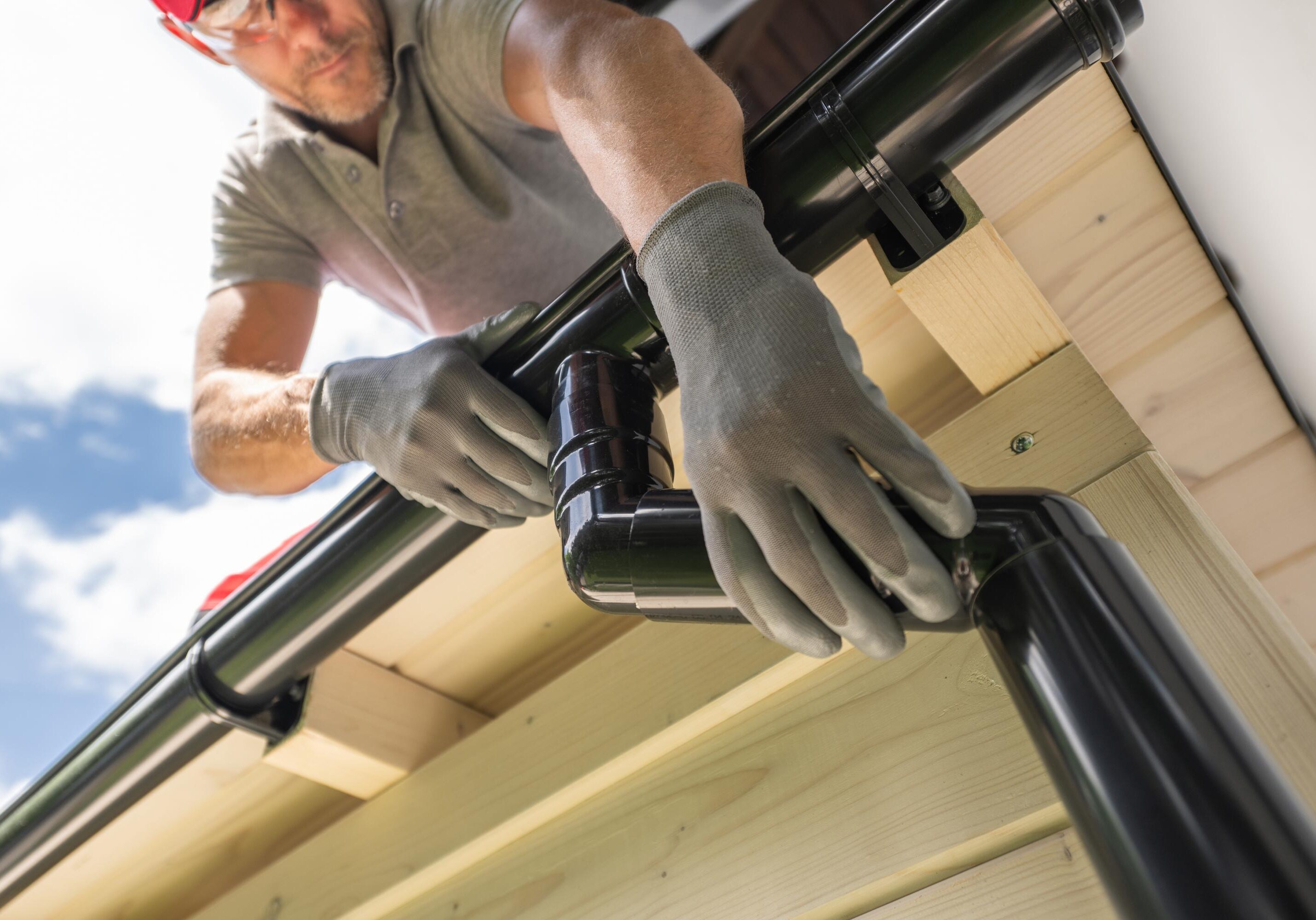 Man installing black rain gutter on roof.