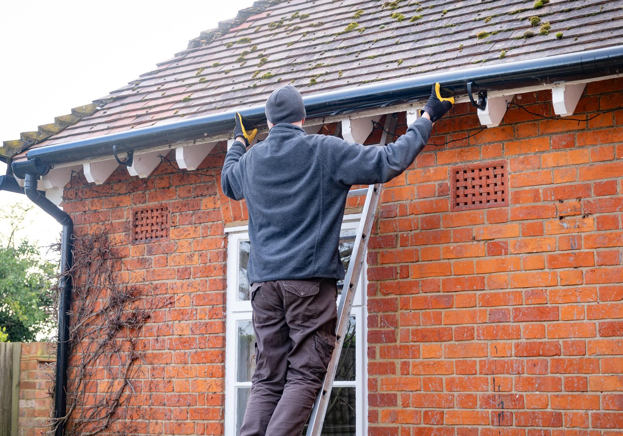 Man on ladder cleaning house gutters.